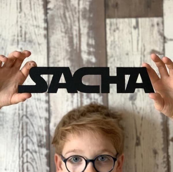 Garçon blond aux yeux bleus avec des lunettes tenant un écriteau noir "Sacha" écrit avec la typographie de Star Wars.